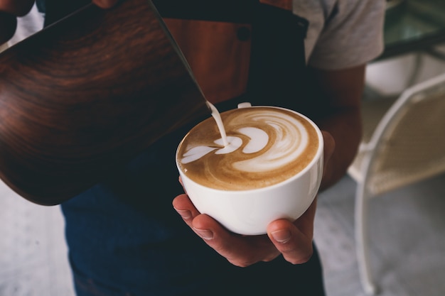 Front view barista pours milk into a cup of coffee