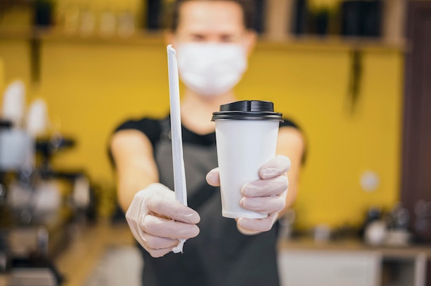 Front view of barista with medical mask holding cup and straw