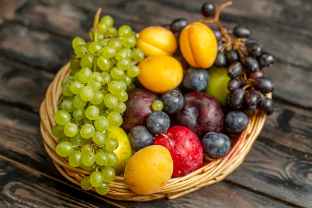 Front view basket with fruits mellow and sour fruits such as grapes apricots plums on the brown rustic background