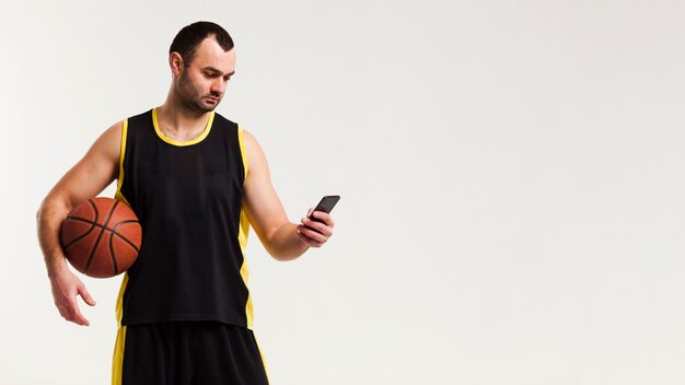 スマートフォンとコピースペースでポーズのバスケットボール選手の正面図