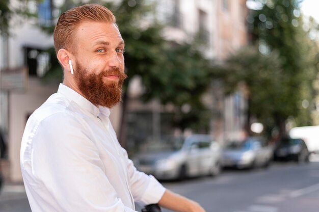 Free photo front view bearded modern man using earbuds with copy space