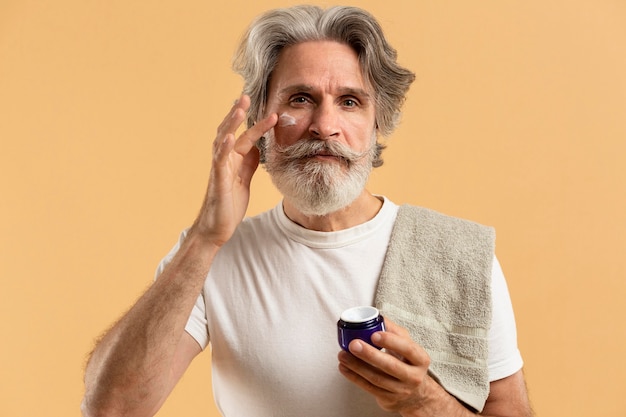 Free photo front view of bearded senior man applying moisturizer