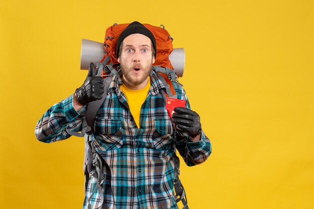 Front view of bearded young man with backpacker holding credit card giving thumb up