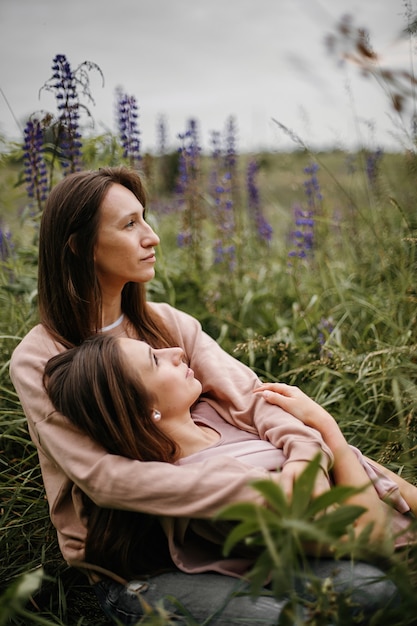 Front view of beautiful brunette girls gay couple sitting in meadow with lupines