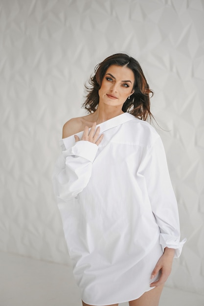 Front view of beautiful brunette woman dressed in white mans shirt, standing on white background