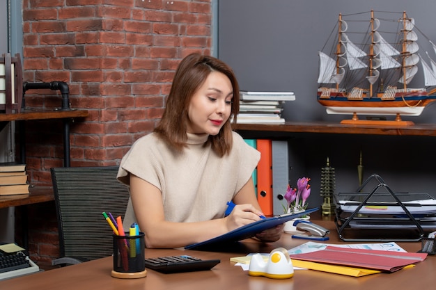 Front view beautiful business woman checking documents sitting at desk in office