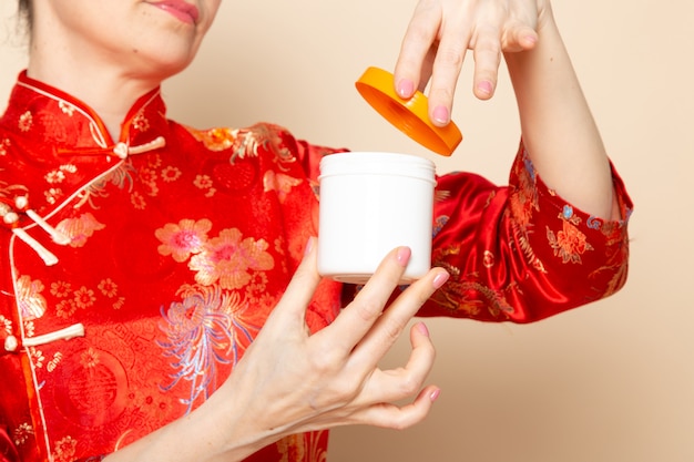 A front view beautiful japanese geisha in traditional red japanese dress with hair sticks posing opening cream can smiling on the cream background ceremony japan