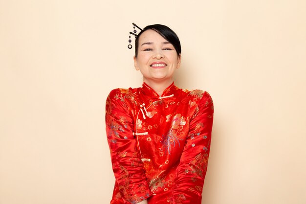 A front view beautiful japanese geisha in traditional red japanese dress with hair sticks posing smiling happy on the cream background ceremony japan