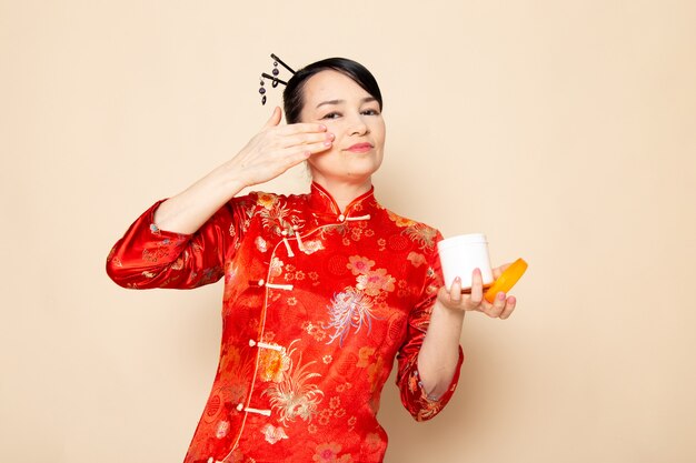 クリームを使用してポーズをとって髪棒でポーズをとって伝統的な赤い和服で正面の美しい日本の芸者は、クリーム色の背景に臭いがすることができます。