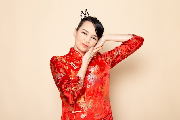 Free photo a front view beautiful japanese geisha in traditional red japanese dress with hair sticks posing with her hands on the cream background ceremony entertaining japan east