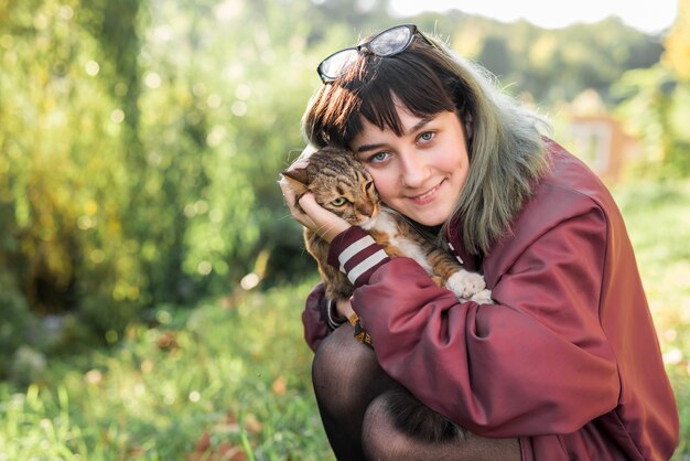 Front view of beautiful woman hugging her tabby cat in park