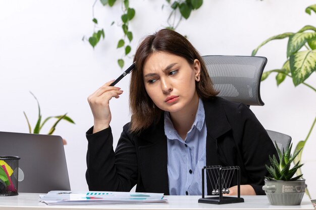 A front view beautiful young businesswoman in black jacket and blue shirt thinking in front of table business job office