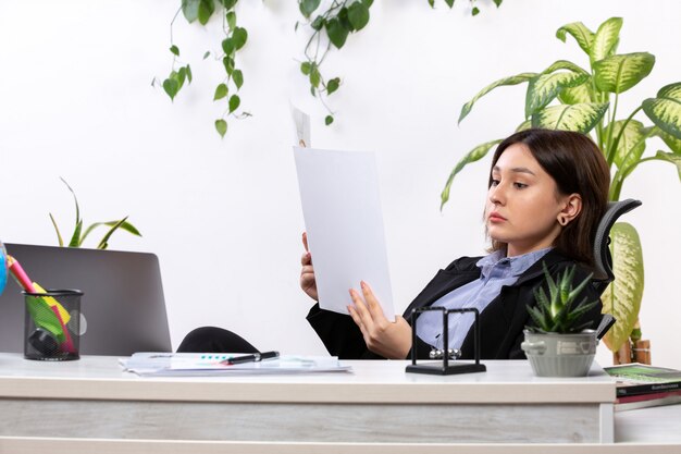 A front view beautiful young businesswoman in black jacket and blue shirt working with documents in front of table business job office