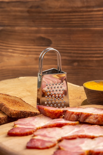 Fette di becon vista frontale su tagliere per pane grattugia su superficie di legno