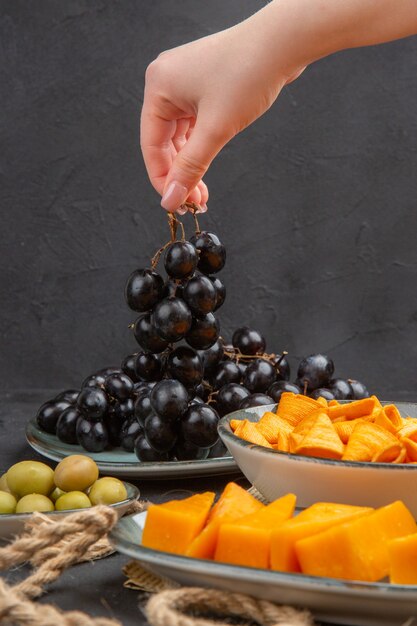 Front view of best delicious snacks on an old newspaper rope and hand holding black grape