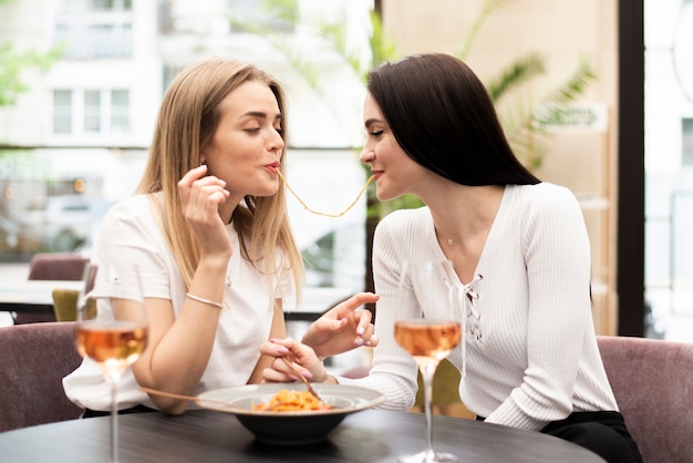 Front view best friends eating the same spaghetti noodle