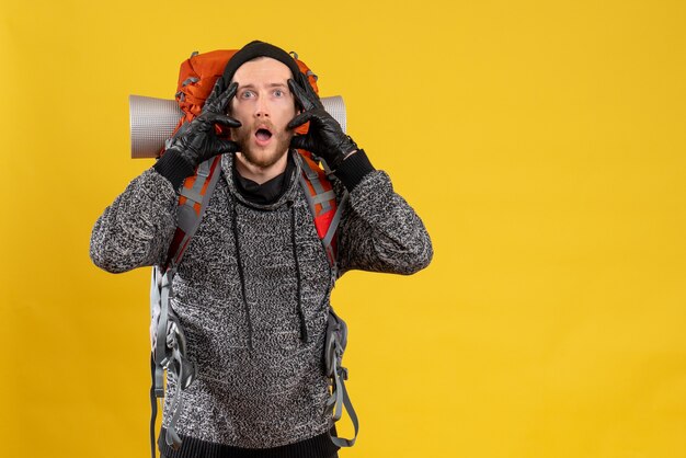 Front view of bewildered male hitchhiker with leather gloves and backpack looking at front