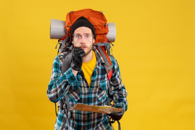 Front view of bewildered young tourist with leather gloves and backpack holding map