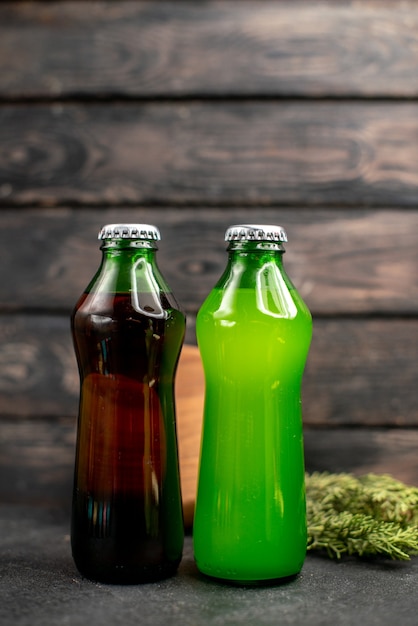 Бесплатное фото Вид спереди черные и зеленые соки в бутылках, деревянная доска на деревянном столе