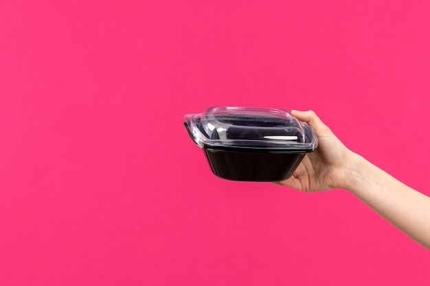 Free photo a front view black bowl hand holding black bowl female hand pink background color cutlery kitchen