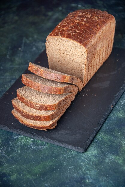 Front view of black bread slices on dark color board on mixed colors distressed background