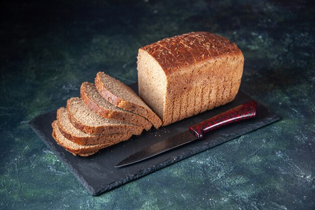 Front view of black bread slices knife on dark color board on mixed colors distressed background