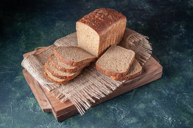 Front view of black bread slices on nude color towel on cutting boards on blue background