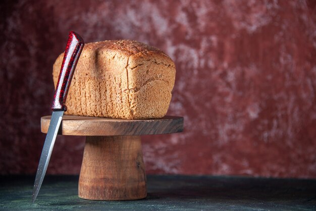 木の板の黒いパンのスライスと混合色の苦しめられた背景の右側のナイフの正面図
