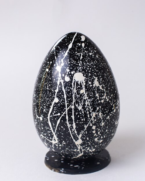 Front view black chocolate egg in white speckled on stand