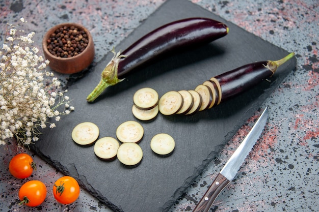 front view black eggplants sliced and whole on cutting board blue background