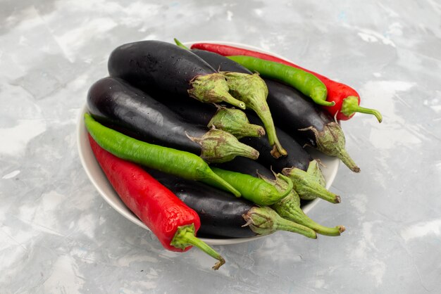 Front view of black eggplants with peppers on the light desk