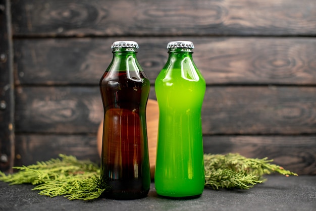 Вид спереди черные и зеленые соки в бутылках, древесная плита, сосновые ветки