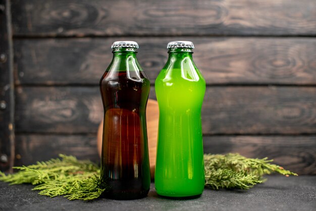 Front view black and green juices in bottles wood board pine tree branches