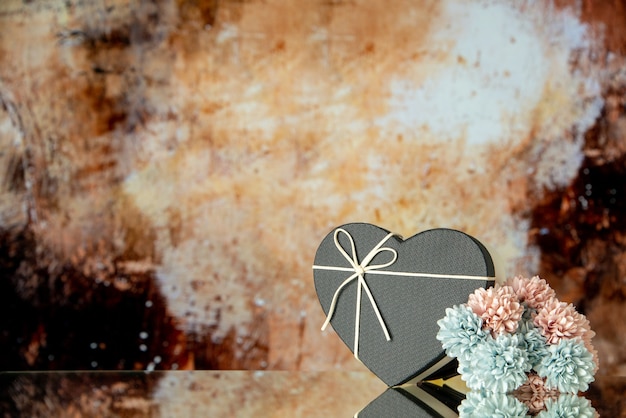 Front view of black heart box colored flowers on brown abstract background