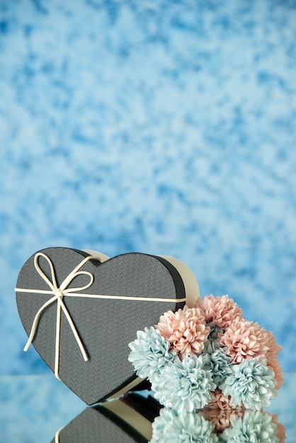 Front view of black heart shaped box colored flowers on blue blurred