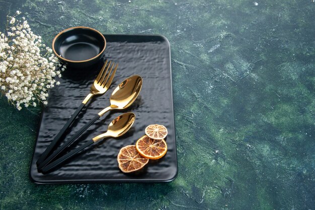 вид спереди черная тарелка с золотыми столовыми приборами на темном фоне