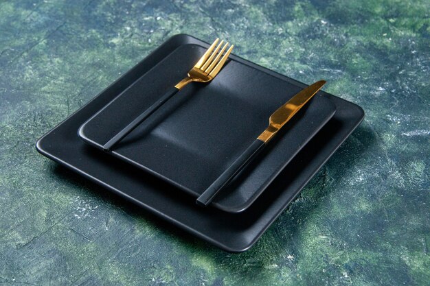вид спереди черные тарелки с золотой вилкой и ножом на темном фоне