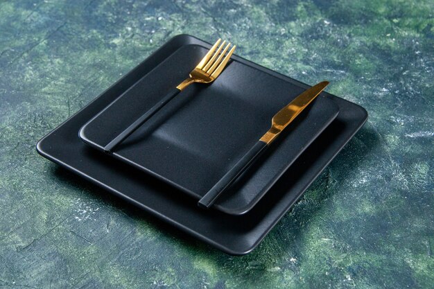 front view black plates with golden fork and knife on dark background