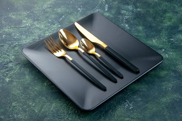 front view black plates with golden spoons knife and fork on dark background
