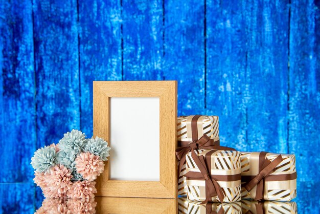 Front view of blank picture frame holiday presents flowers on blue wooden background