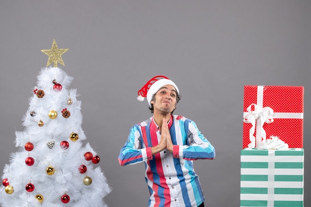 Front view blessed man making praying sign near white xmas tree