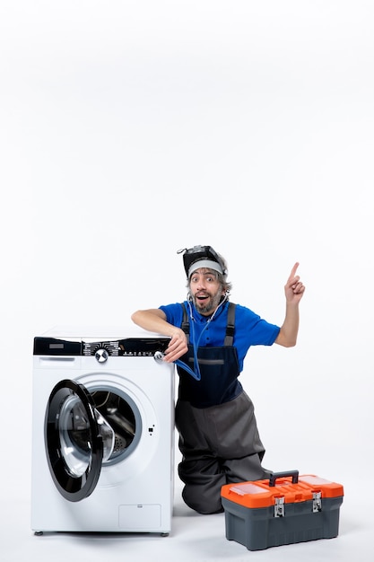 Free photo front view blessed repairman sitting near washing machine raising his hand on white space