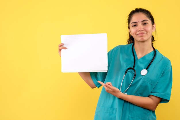 Front view blissful female doctor pointing at papers on yellow background