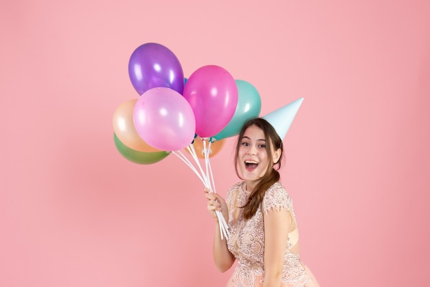 Front view blissful girl with party cap holding colorful balloons