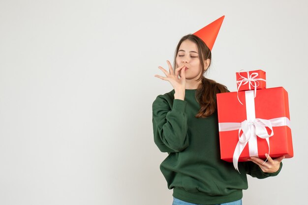 Front view blissful girl with party cap holding gifts making chef tasty gesture