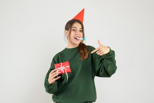 Front view blissful girl with party cap pointing at her xmas gift