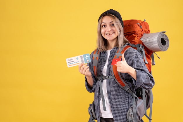 親指をあきらめてチケットを保持しているバックパックと至福の旅行者の女性の正面図