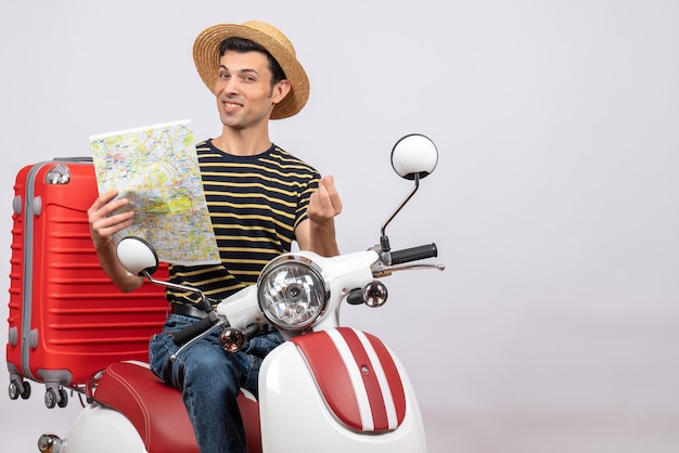 Front view of blissful young man with straw hat on moped holding map