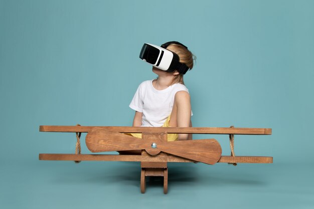 front view blonde boy in white t-shirt playing vr goggles on the blue floor
