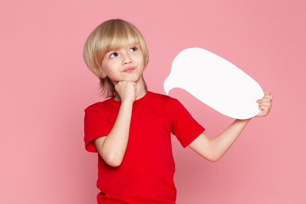 Free photo a front view blonde haired boy in red t-shirt holding white sign on the pink backgorund